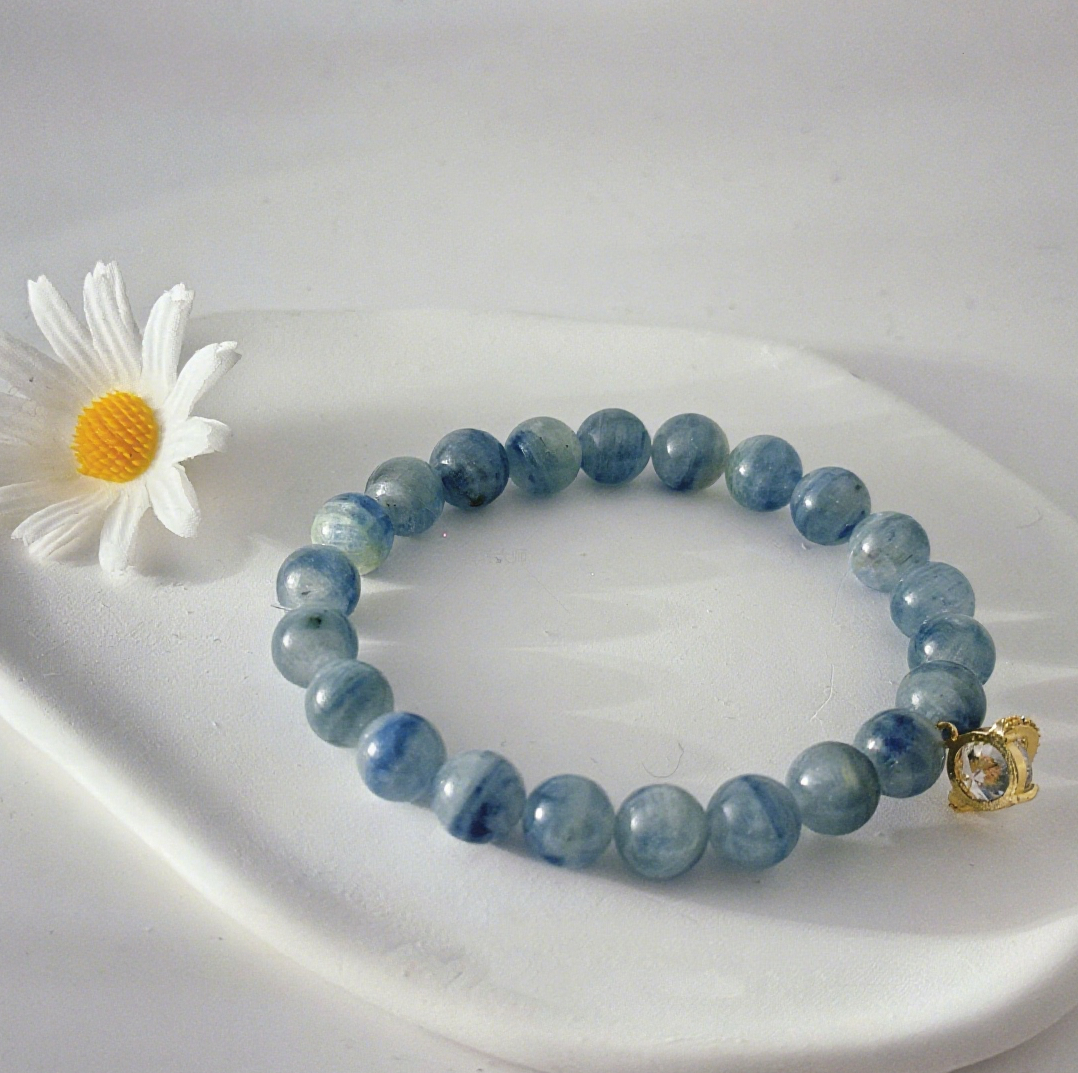 A cat's eye blue crystal bracelet made of blue crystal beads, paired with a gold-inlaid accessory, placed on an irregular white tray with a white daisy beside it, and set against a white background, showcasing its fresh and elegant crystal jewelry texture and design.